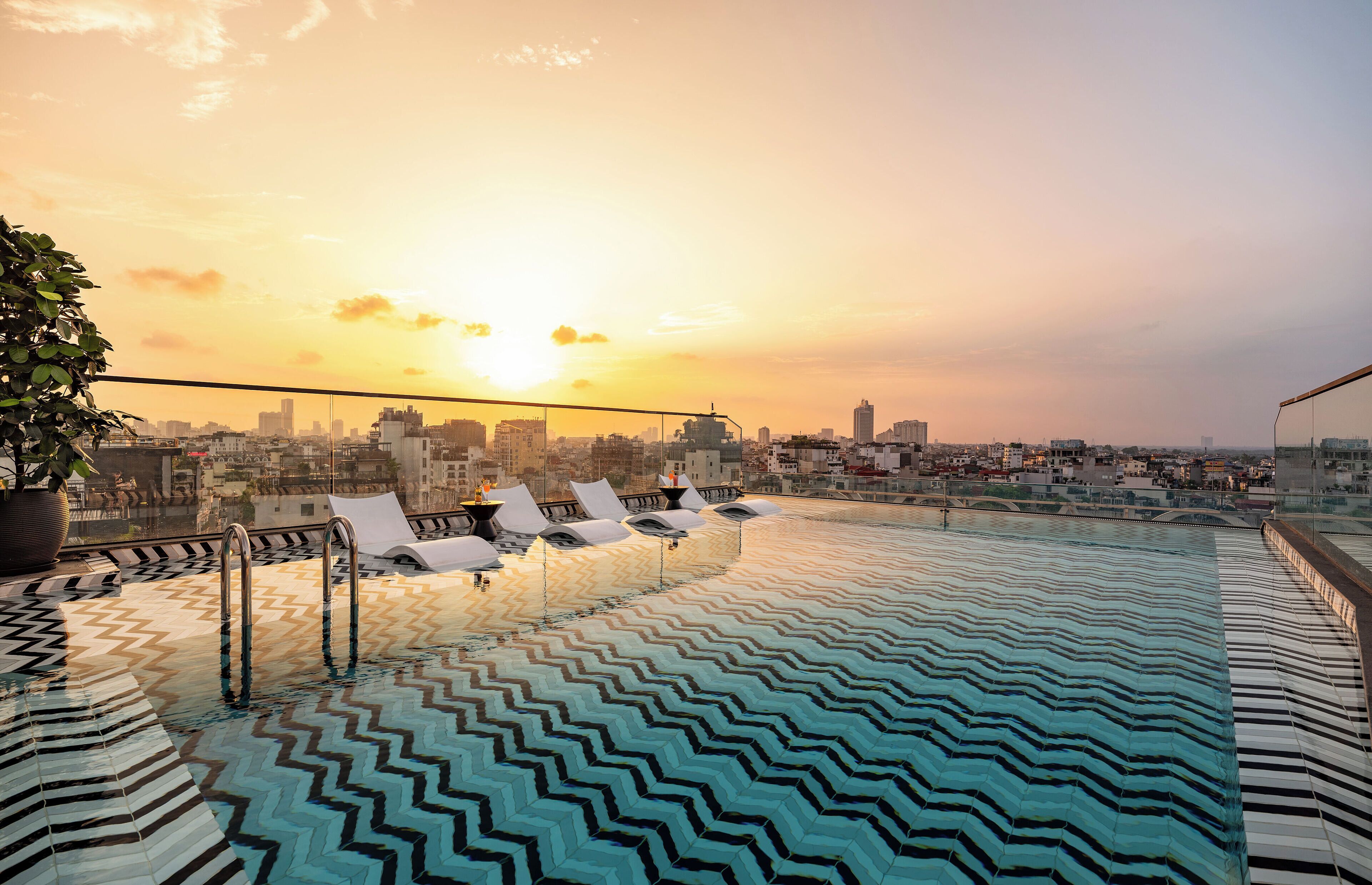A rooftop infinity pool with a cityscape view at sunset.