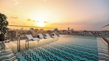 A rooftop infinity pool with a cityscape view at sunset.