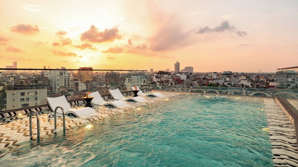 A rooftop pool with clear water, surrounded by lounge chairs, and a cityscape view in the background. - CLASSYC Hotel (Hanoi)