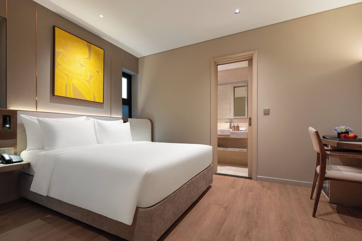 A modern hotel room with a large bed, a desk, and a bathroom visible through an open door.