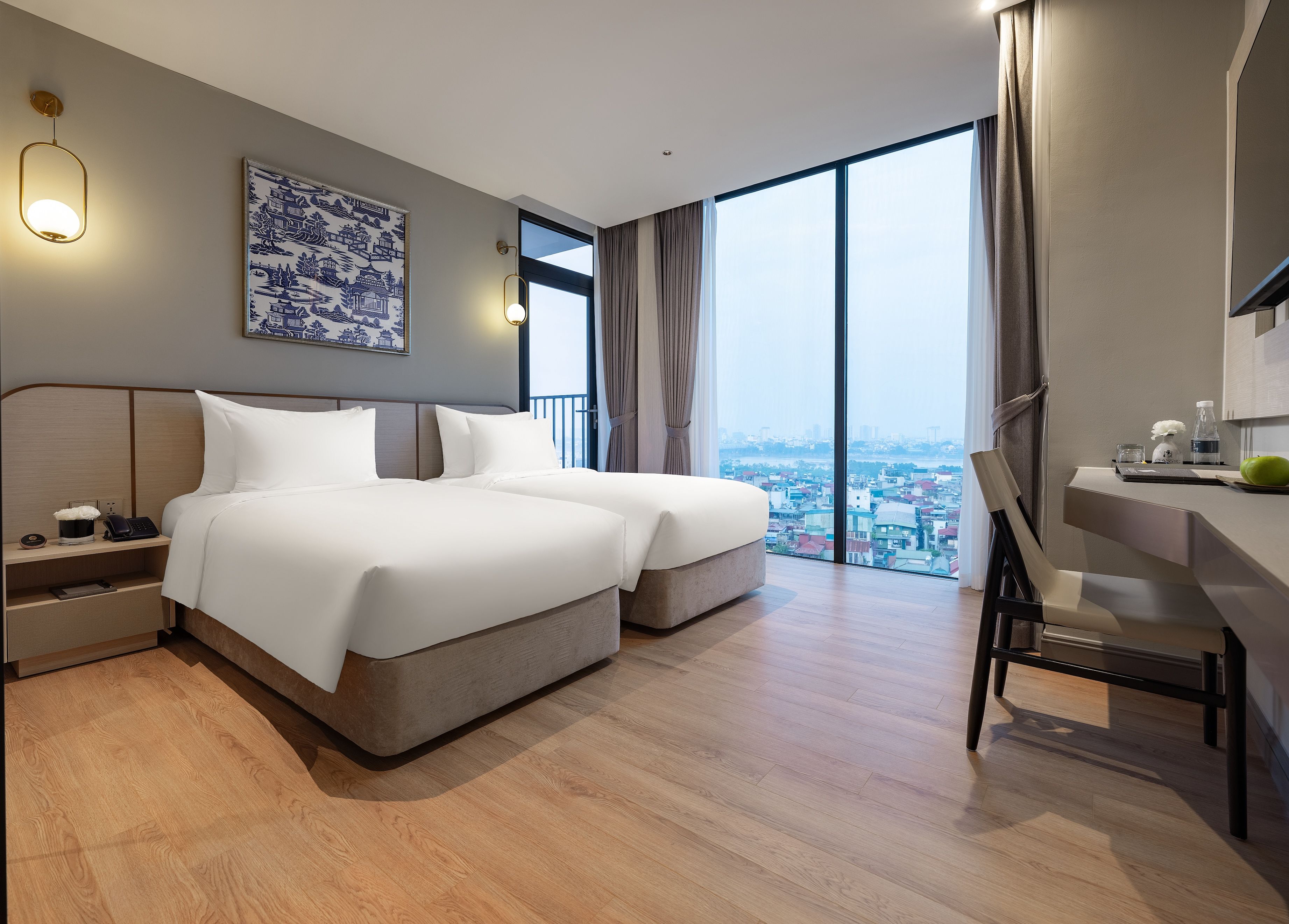 A modern hotel room with a large bed, bedside tables, a desk, and a view of the city.