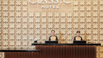 A reception desk at CLASSYHC HOTEL with a patterned wall and two staff members behind it.