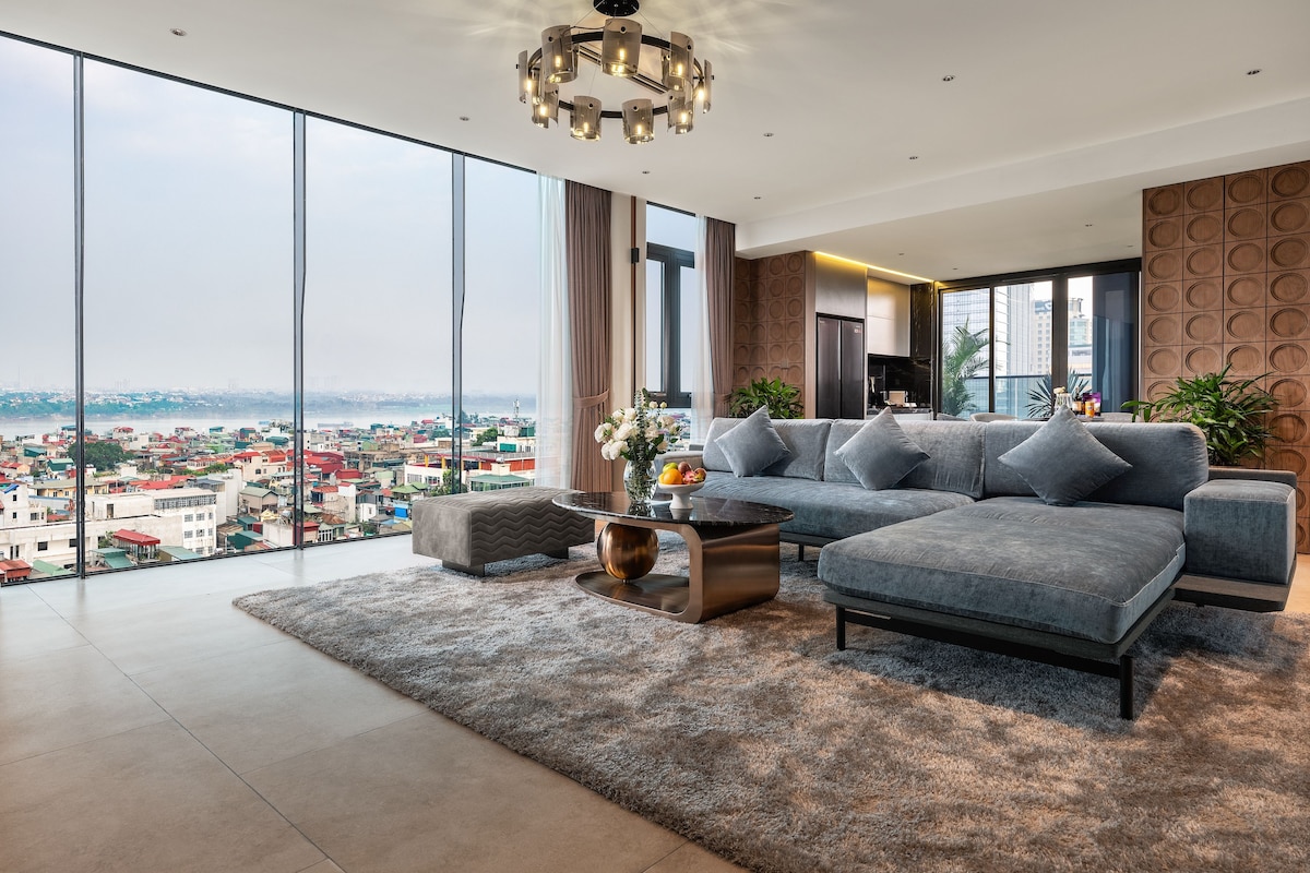 A modern living room with a large sofa, a coffee table, and a view of a cityscape through floor-to-ceiling windows.