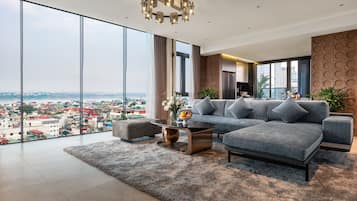 A modern living room with a large sofa, a coffee table, and a view of a cityscape through floor-to-ceiling windows.