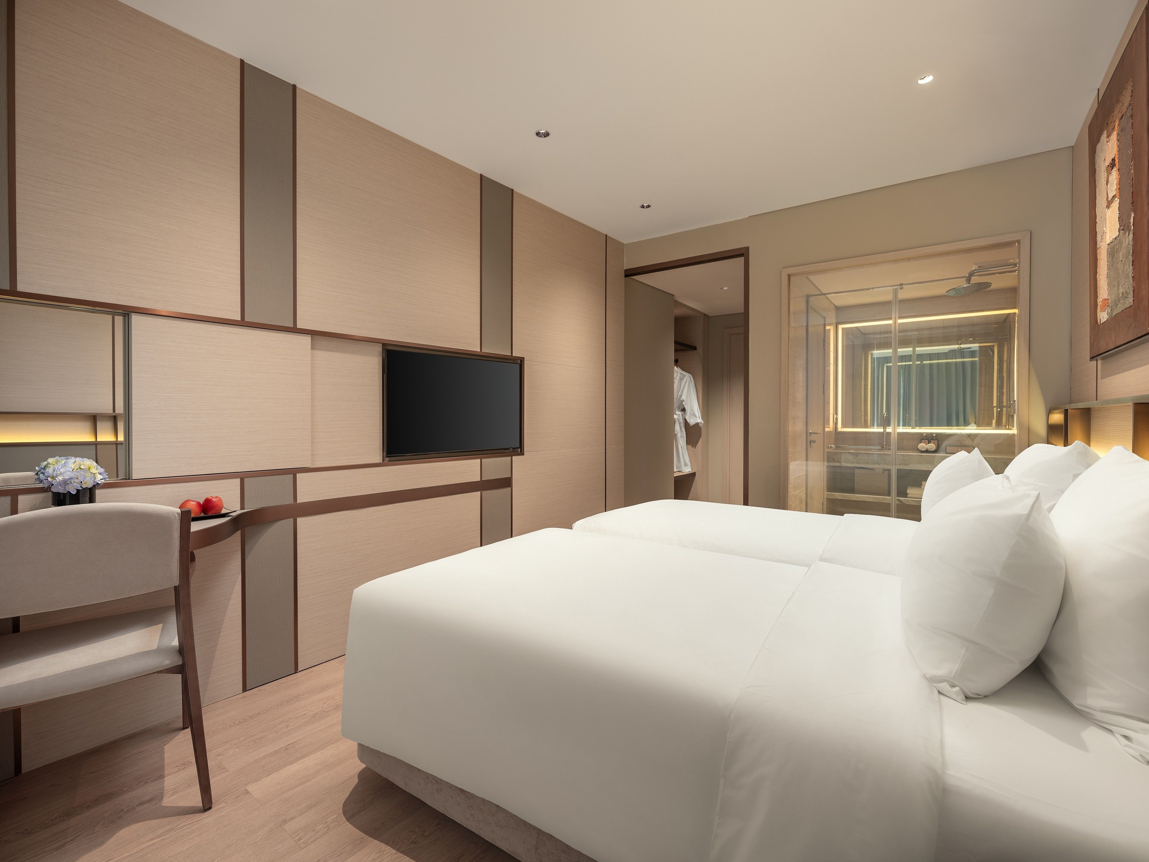 A modern hotel room with a large bed, a flat-screen TV, a seating area with a chair, and a walk-in closet.