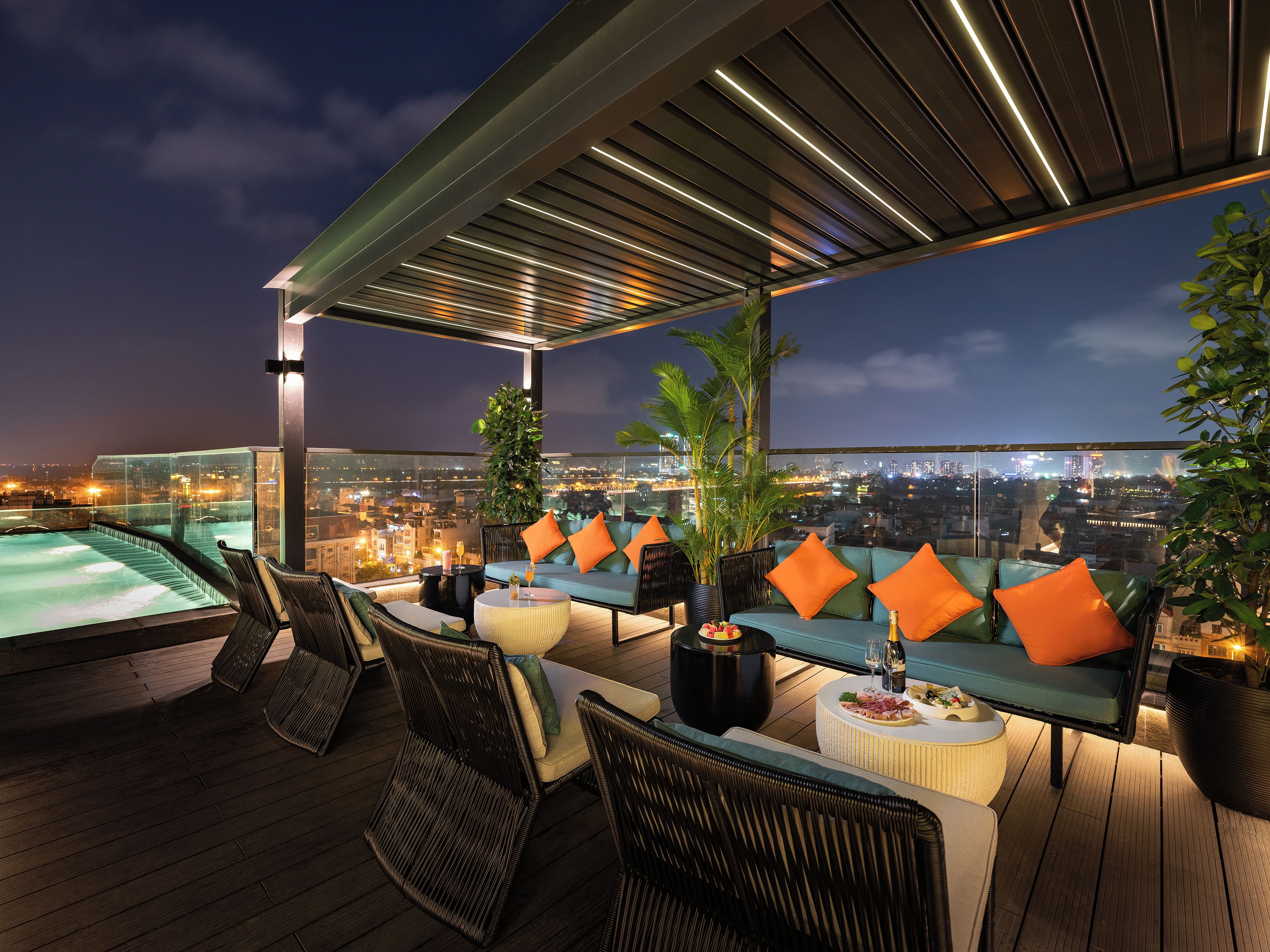 A rooftop terrace with a hot tub, seating area, and a city view at night.