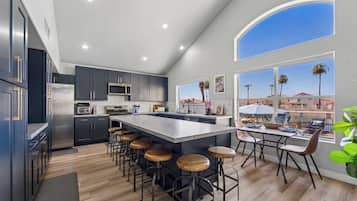 Una cocina moderna con una isla grande, taburetes de bar y vistas a palmeras a través de las ventanas.