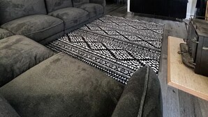 Un salon moderne avec un canapé d’angle, un tapis à motifs et des œuvres d’art décoratives accrochées au mur.