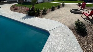 Un jardin à l’arrière d’une maison, avec une piscine, un espace patio doté de chaises rouges et une pelouse bien entretenue.