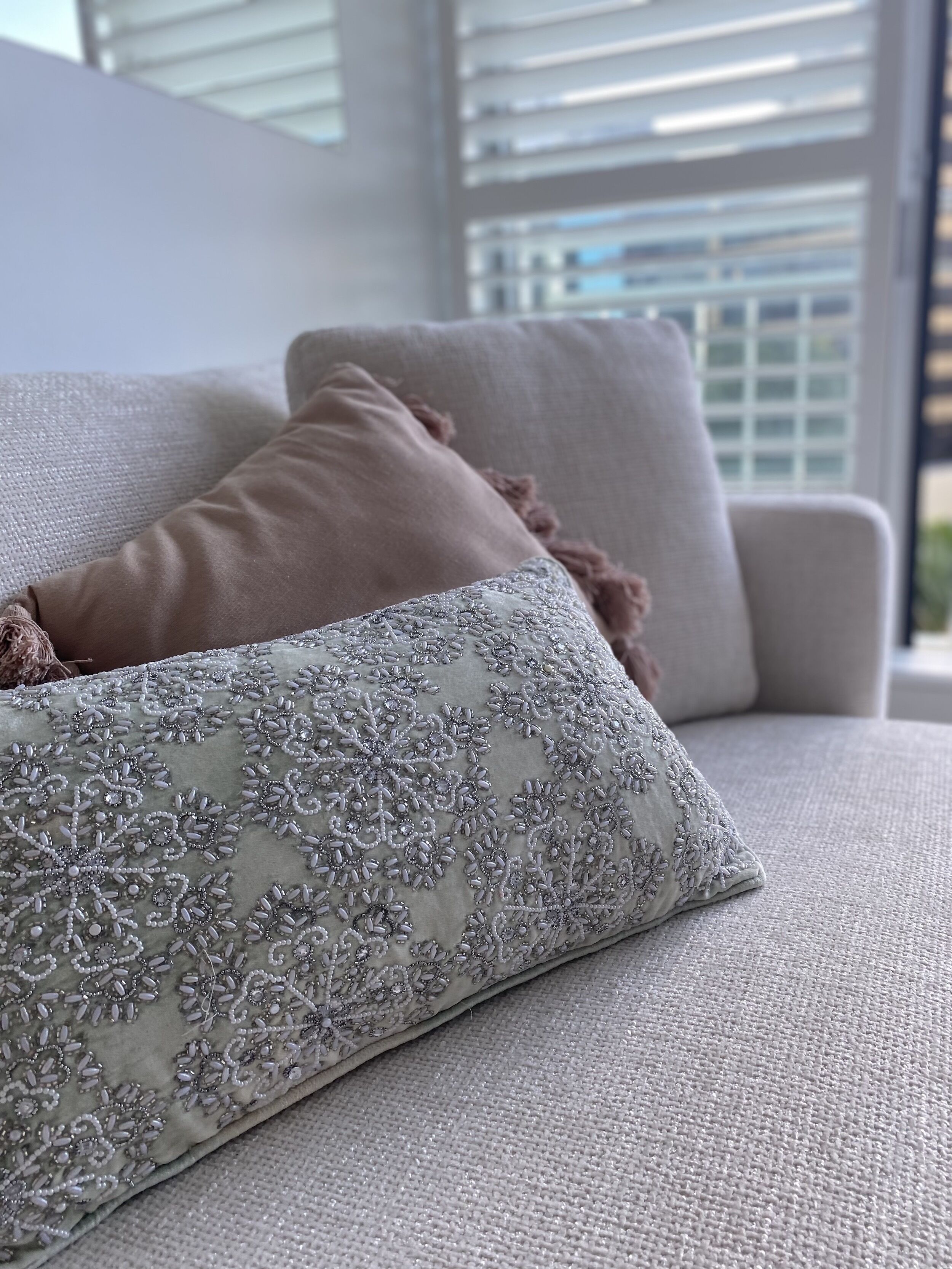 A beige sofa with two pillows, one plain and one with silver embroidery.
