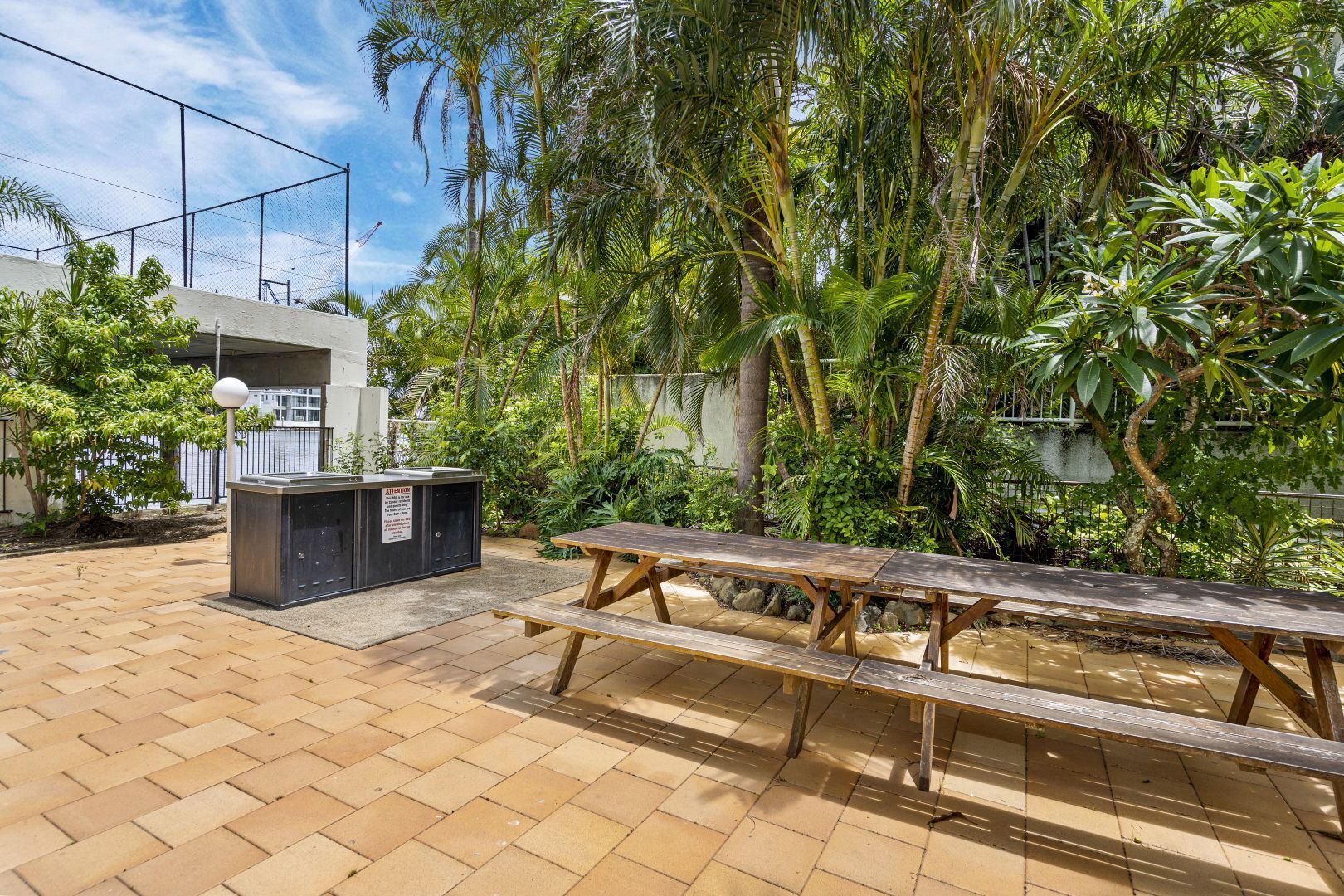 Un patio al aire libre con una mesa de picnic de madera y un cubo de basura.