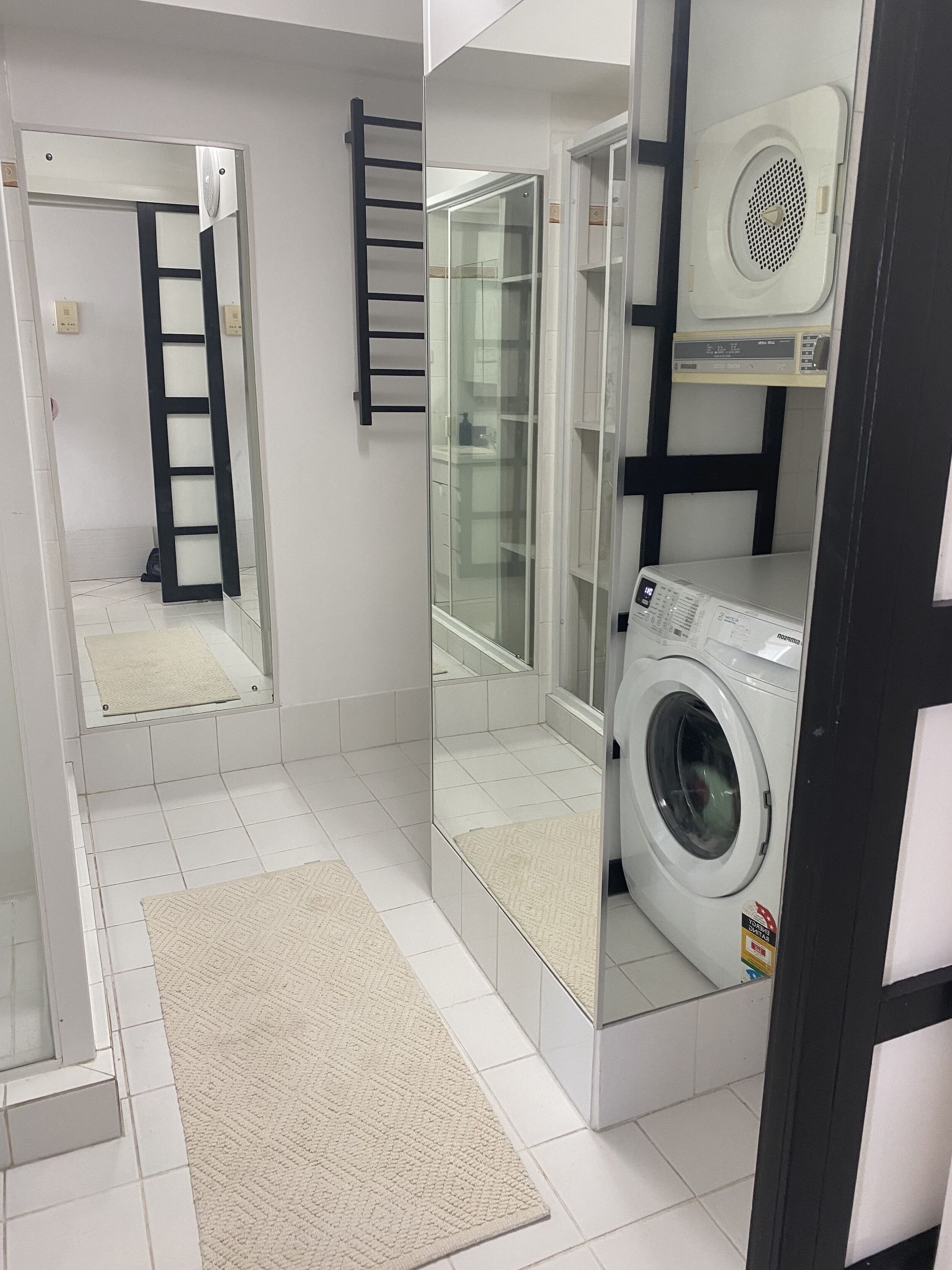 A compact laundry room with a washing machine, a drying machine, a mirror, and a towel rack.