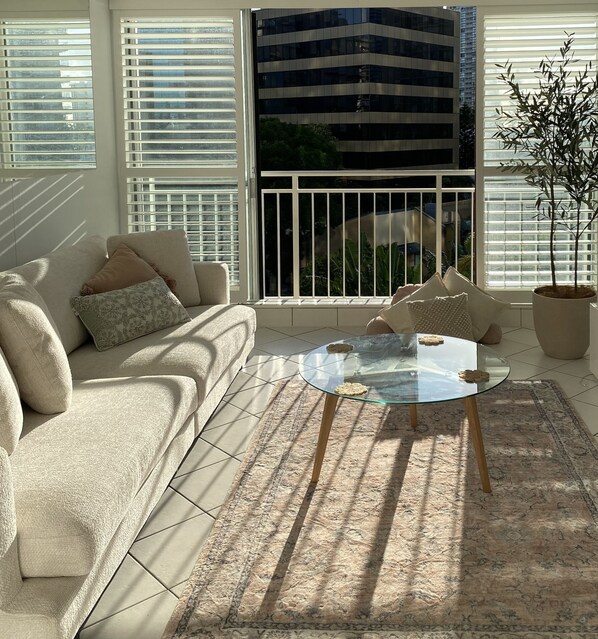 A modern living room with a beige sofa, a glass coffee table, and a potted plant. - Condor Surfers - Coastal Letting Co (Surfers Paradise)