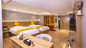 Habitación de hotel con dos camas, un escritorio, una silla, un armario y un baño visible a través de una puerta de cristal.