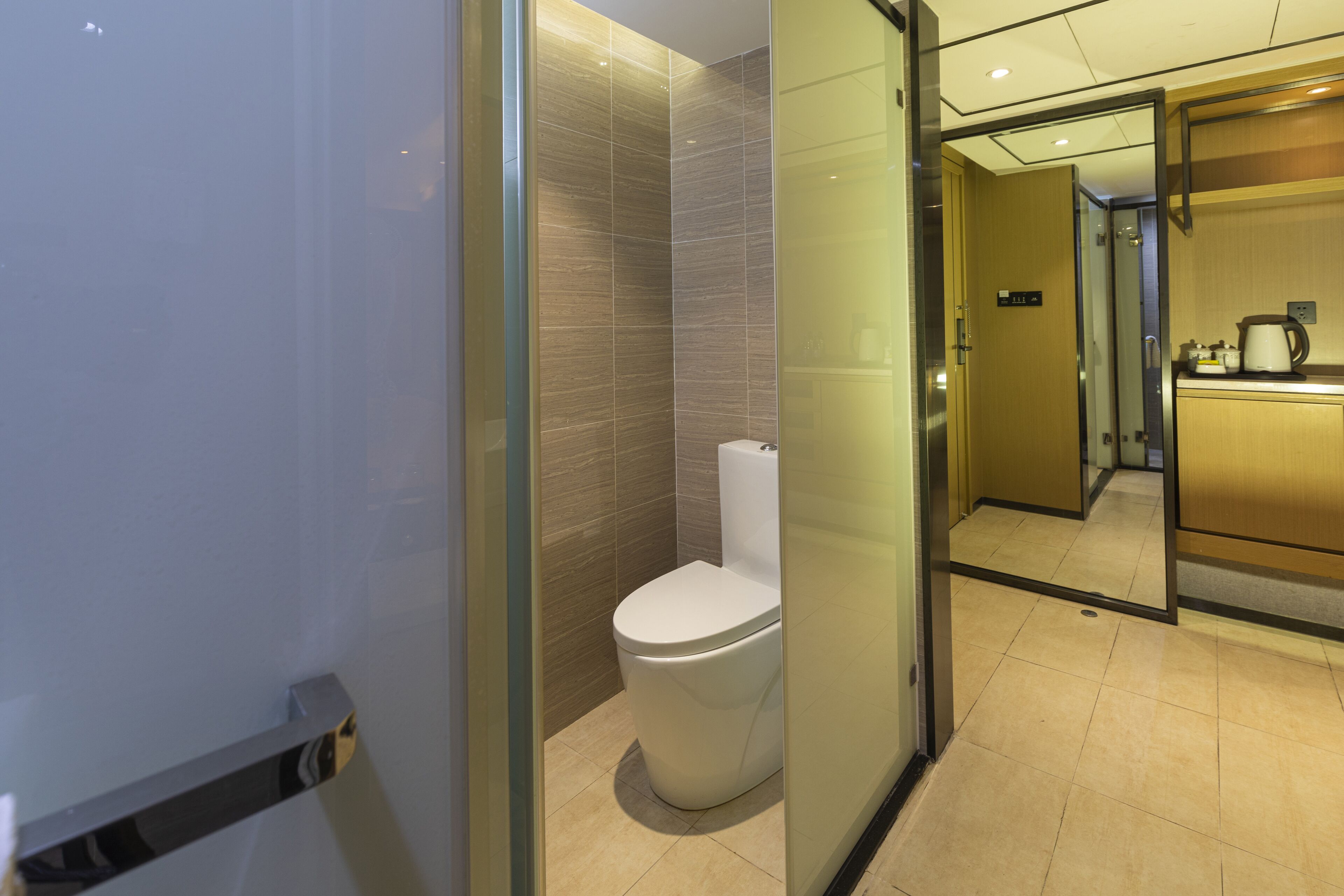 A modern bathroom with a toilet, a glass partition, and a visible kitchen area in the background.