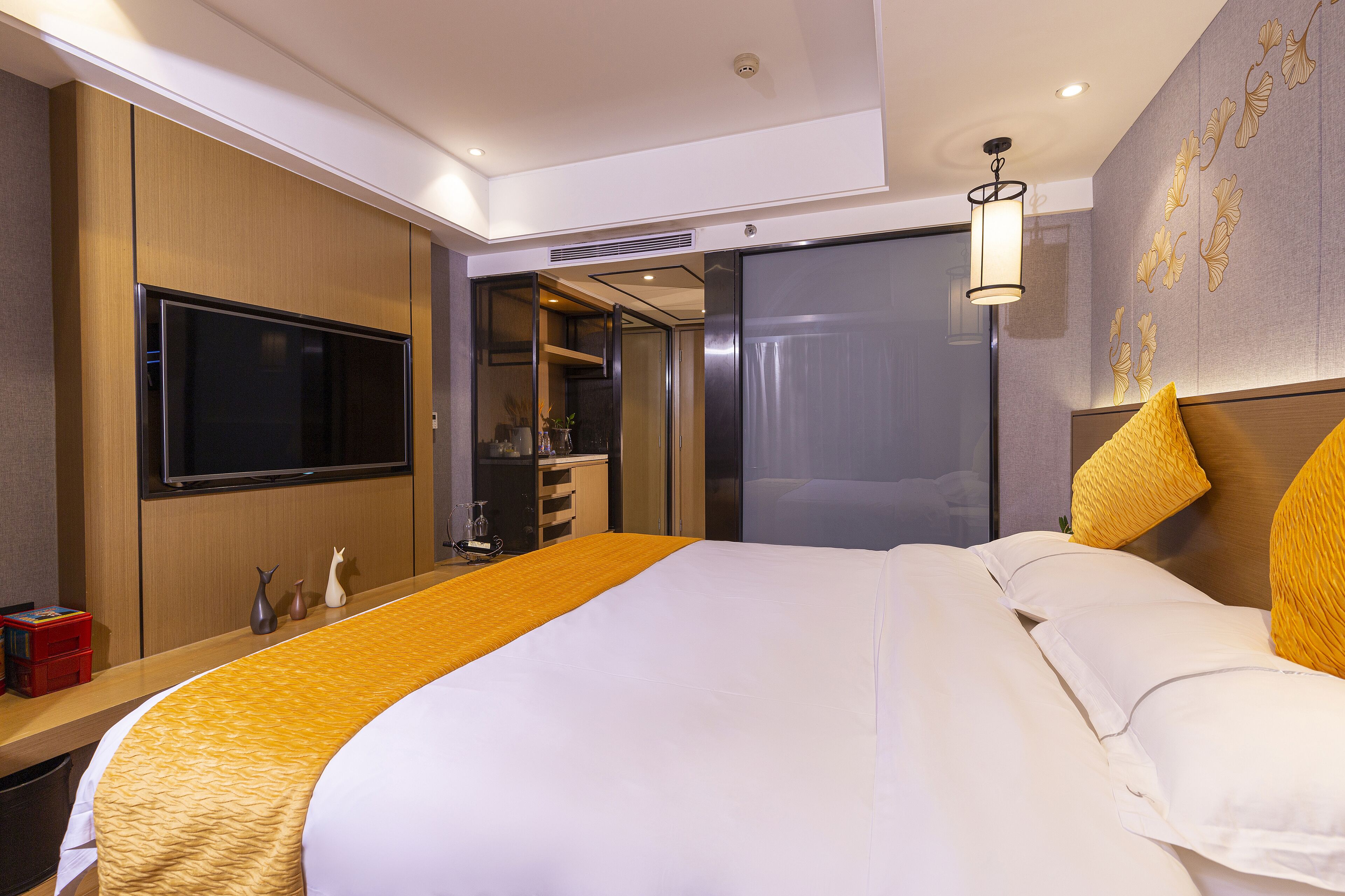 A hotel room with a large bed, a TV on the wall, a wardrobe, a mirror, and a bedside table.