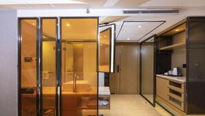Una habitación de hotel moderna con un separador de vidrio, un lavamanos, un espejo y un armario.