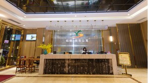 Mostrador de recepción de hotel con una mampara de cristal, una recepcionista y un cartel.