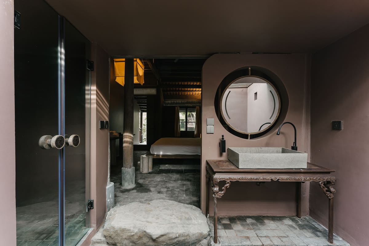 A bathroom with a round mirror, a sink, and a stone bench.