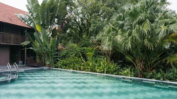 Una piscina con diseño en forma de estampada, rodeada de exuberante vegetación tropical y un edificio con tejado de tejas rojas.