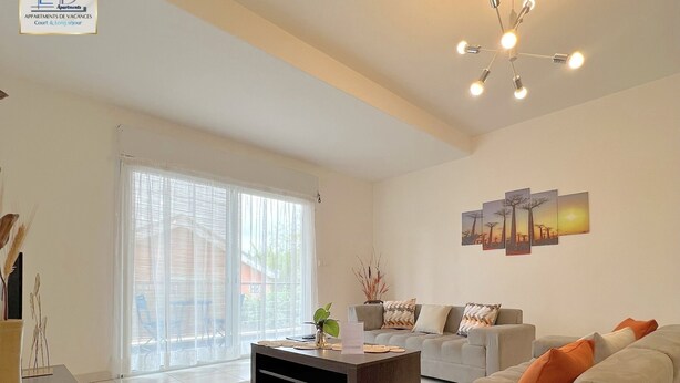A spacious living room with a large window, a sofa, a coffee table, and a chandelier. -  E&D Apartment with balcony, Quiet and Secure Ideal For Families (Tananarive)