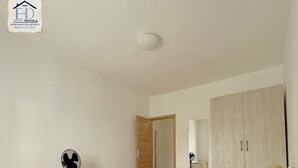 A bedroom with a bed, a bedside table, a fan, a wardrobe, and a mirror. -  E&D Apartment with balcony, Quiet and Secure Ideal For Families (Tananarive)