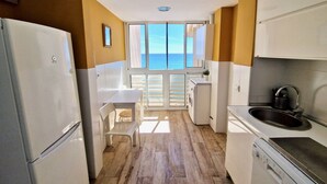Une cuisine compacte avec vue sur la mer, comprenant un lave-linge, un évier et un coin repas.