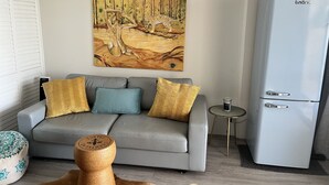 Ein modernes Wohnzimmer mit einem grauen Sofa, gemusterten Kissen, einem Holztisch und einem Gemälde von einem Leoparden sowie einem weißen Kühlschrank.
