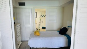 Ein Schlafzimmer mit Bett, Kommode, Duschbereich und einer Tür zu einem anderen Raum.