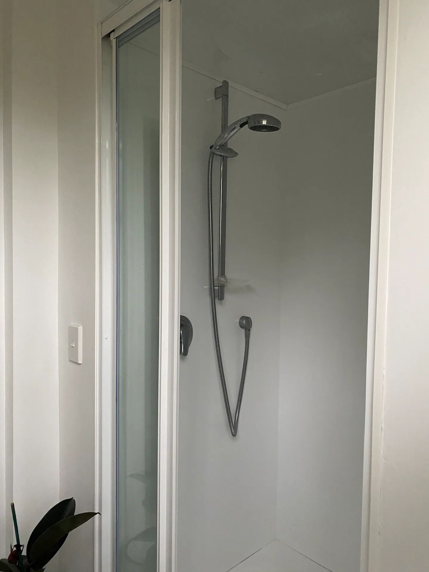 A shower with a glass door, a handheld showerhead, and a wall-mounted faucet.