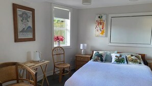 Un dormitorio con una cama, dos sillas, una mesita, una ventana con flores y una pared con un cartel.