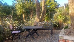 Un patio con una mesa y sillas, rodeado de árboles y plantas.