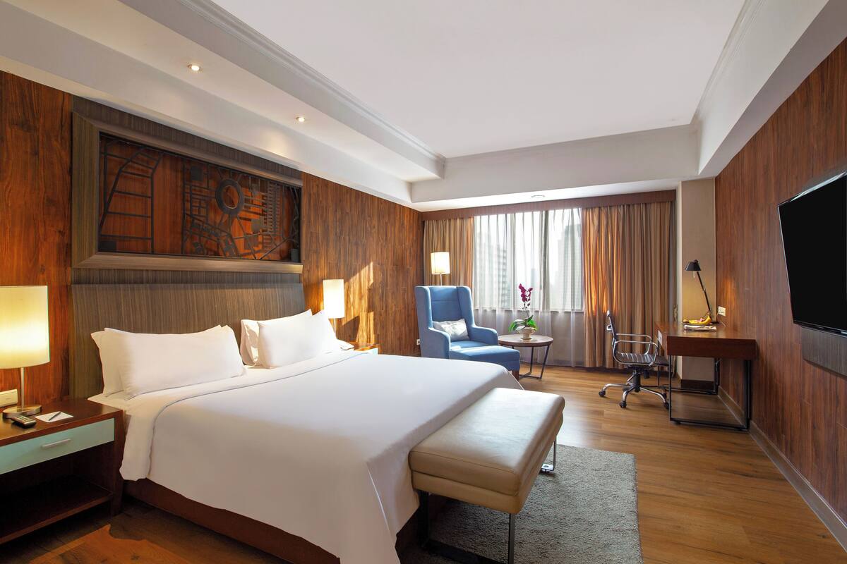 Ein Hotelzimmer mit einem großen Bett, einem Schreibtisch, einem Stuhl, einem Fernseher und einem Fenster mit Vorhängen.