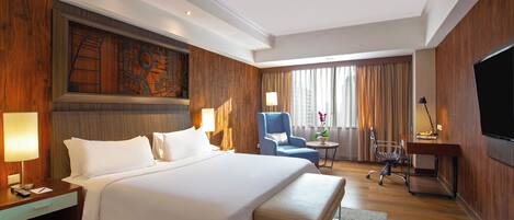 A hotel room with a large bed, a desk, a chair, a TV, and a window with curtains.