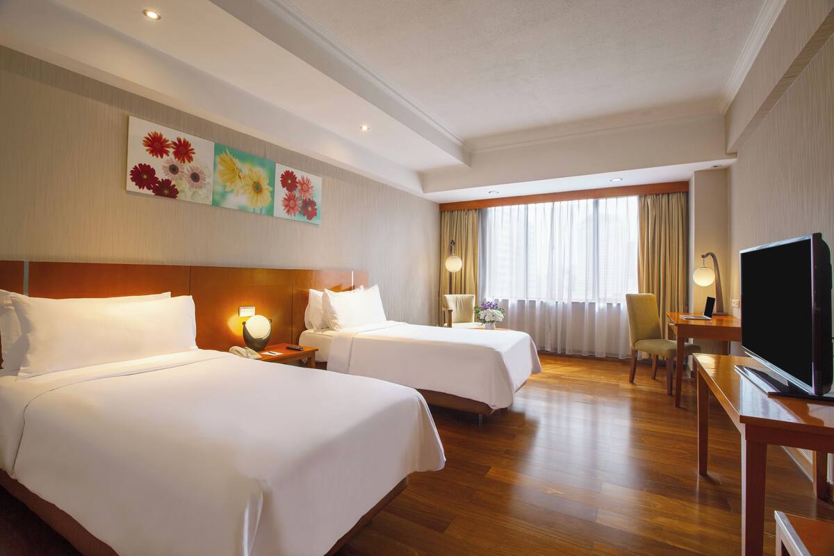 Ein Hotelzimmer mit zwei Betten, einem Fernseher, einem Schreibtisch und einem Fenster mit Vorhängen.
