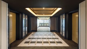 Un pasillo moderno de hotel con alfombra estampada, ventanas amplias y una lámpara en el techo.