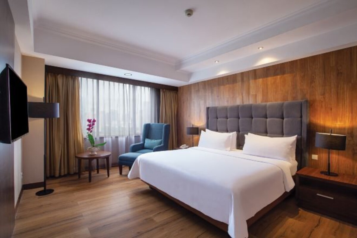 Habitación de hotel con una cama grande, un escritorio, una silla, un televisor y una ventana con cortinas.