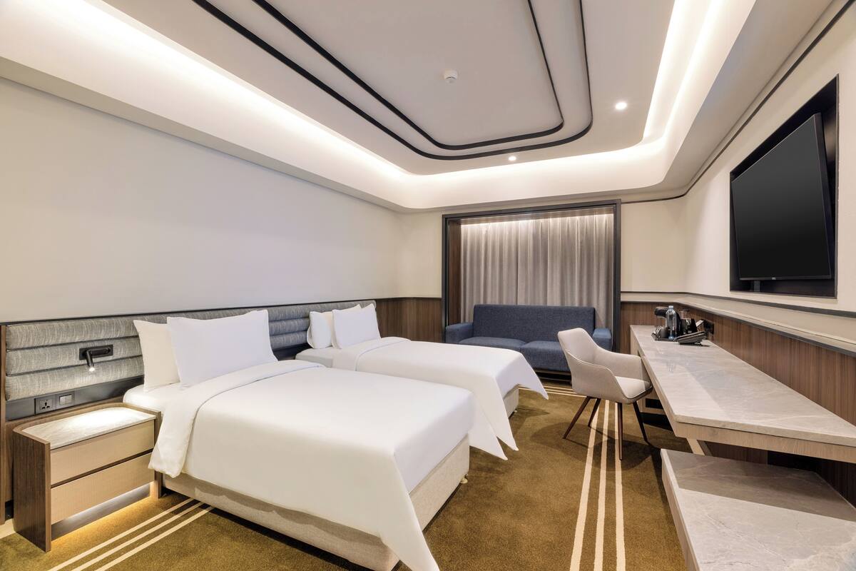 Ein modernes Hotelzimmer mit zwei Betten, einem Schreibtisch, einem Stuhl und einem Fernseher.