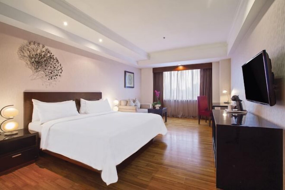 A hotel room with a large bed, a desk with a chair, a television, and a decorative wall piece.