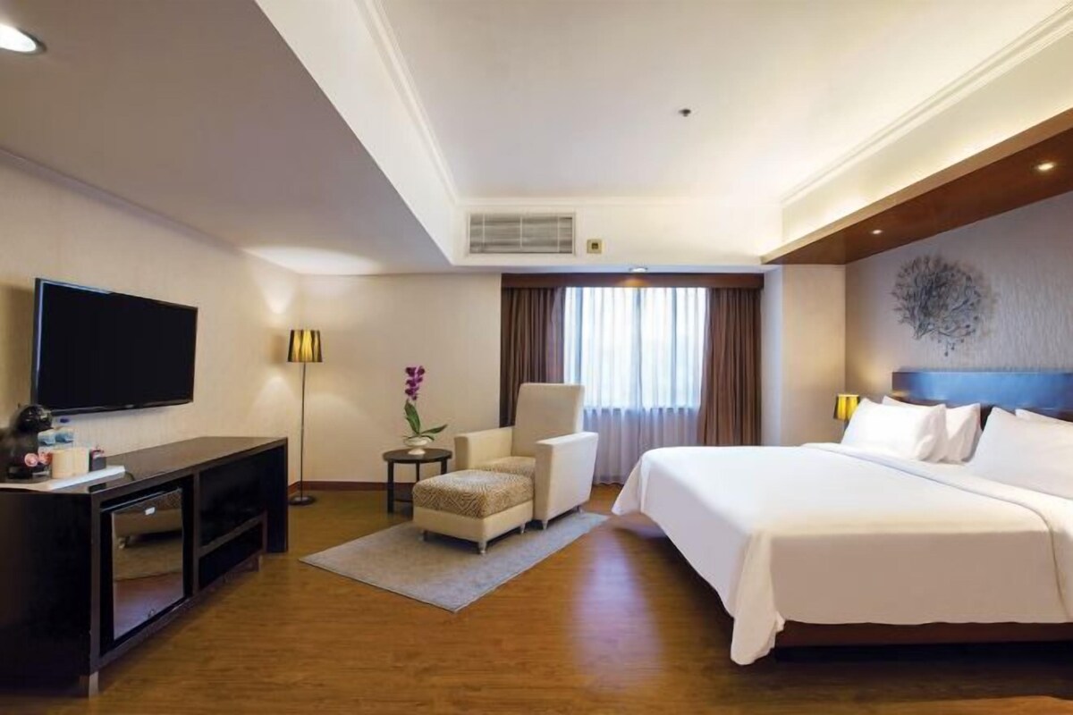 A hotel room with a large bed, a TV, a desk, and a chair.