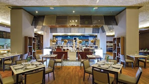 Un restaurante con varias mesas y sillas, una cocina al fondo y un techo con diseño.