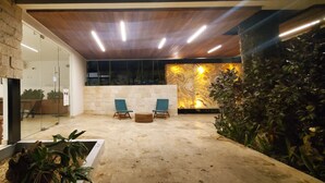 Un intérieur moderne avec un mur en pierre, un plafond en bois et un coin salon comprenant deux fauteuils et une petite table.