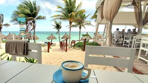 Un café en bord de mer, avec une table et une tasse de café, d’où l’on peut admirer l’océan et les palmiers.