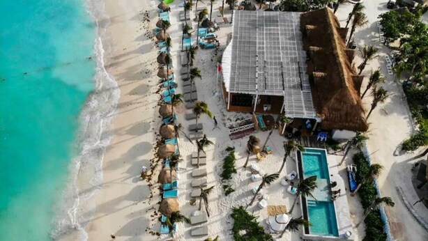 Vue aérienne d’un club de plage avec une piscine, des chaises longues et un bâtiment à toit de chaume.