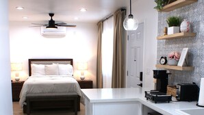 Une chambre d’hôtel compacte comprenant un coin cuisine, un lit et un ventilateur de plafond.