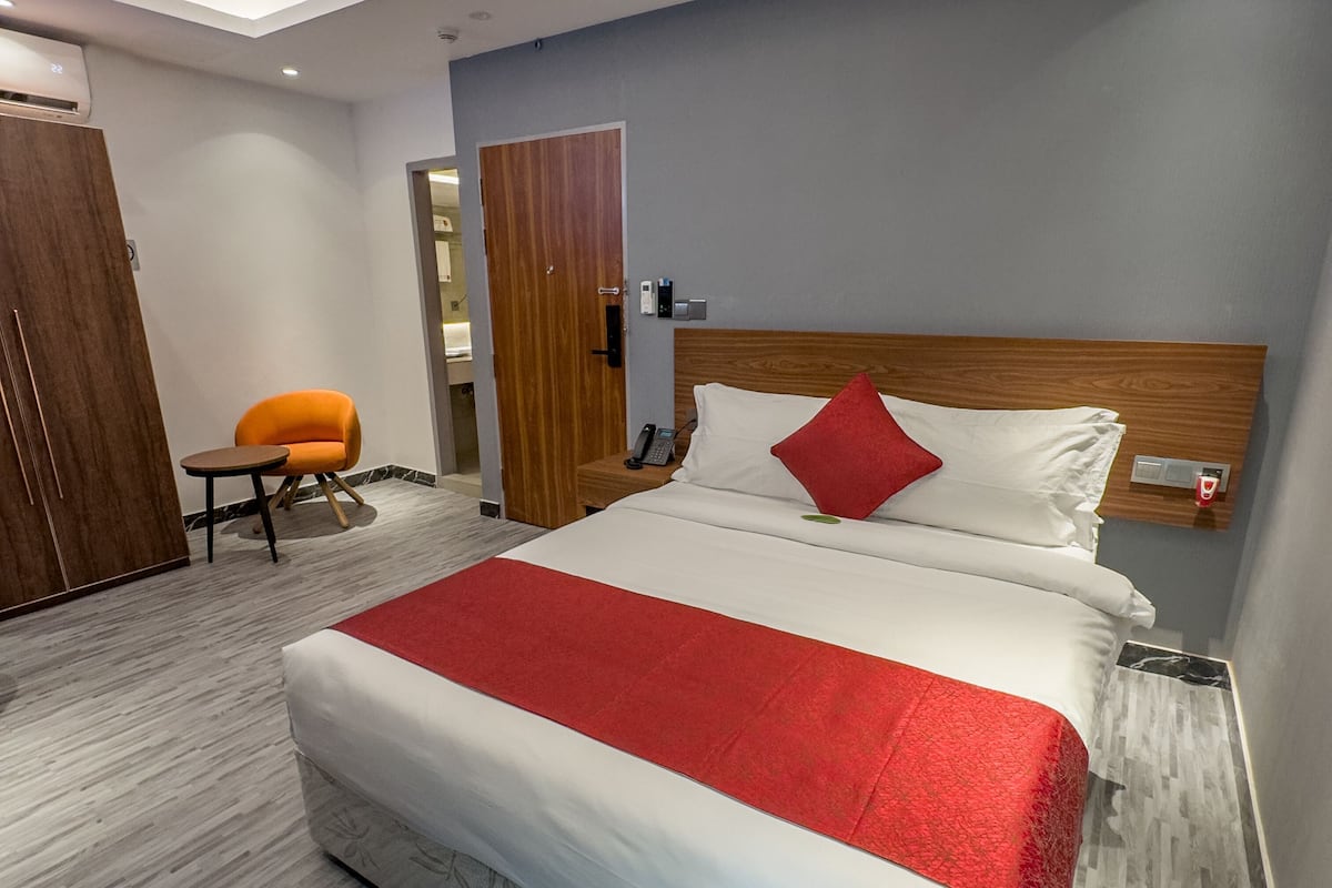 Una habitación de hotel moderna con una cama grande, un cabecero de madera, una mesita con una silla y una pared de acento roja.