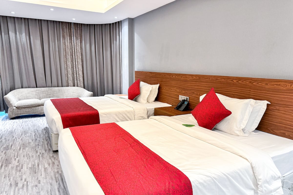 Habitación de hotel con dos camas, un sofá, un teléfono en la mesita de noche y una ventana con cortinas.
