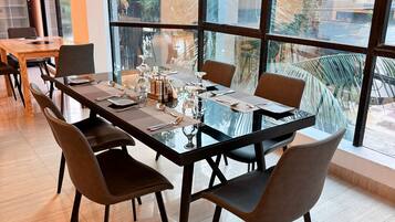 Un comedor moderno con una mesa y sillas de vidrio, grandes ventanales que ofrecen vistas a zonas verdes y edificios.