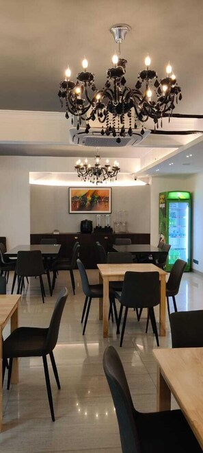 Un comedor moderno con sillas negras, mesas de madera y una araña.