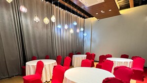 A conference room with round tables and red chairs, wooden floors, and a curtain backdrop. - Hotel omni residency Baridhara (Dhaka)